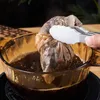 A hand using tongs to hold a tea bag over a pot of hot liquid. Produktbild-Vorschau