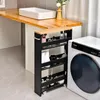 A slim black storage cart with a wood-tone top is placed next to a washing machine in a bathroom or laundry room setting. Podgląd zdjęcia produktu