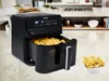 A black air fryer filled with french fries is shown on a kitchen counter, with a bowl of french fries next to it. The background shows a kitchen setting. Produktbild-Vorschau