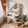 A white vanity table with a mirror and LED lights, filled with makeup and accessories, placed in a room with curtains and a plant. Produktbild-Vorschau