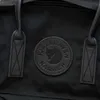 A close-up view of a black Fjällräven Kånken backpack, focusing on the brand's circular logo. Anteprima dell’immagine prodotto