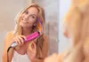 A young woman is styling her hair with a pink hair straightener, adding colorful streaks. Produktbild-Vorschau