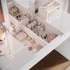 A close-up view of an open drawer of a white vanity table, filled with various makeup and skincare products. Podgląd zdjęcia produktu