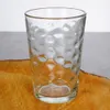 A clear glass with a textured surface sits on a wooden surface. Náhled obrázku produktu