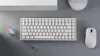 A white mechanical keyboard and a white mouse are placed on a gray surface, with two small decorative glass cubes nearby. Anteprima dell’immagine prodotto