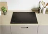 A black electric stovetop is shown on a light wood countertop, with kitchen items in the background. Produktbild-Vorschau