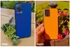 Two smartphones, one blue and one orange, are displayed outdoors with plants and flowers. Produktbild-Vorschau