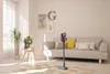 A modern living room with a sofa, a coffee table with plants, and a cordless vacuum cleaner. Produktbild-Vorschau