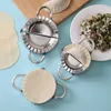 Three stainless steel dumpling makers are arranged on a light blue surface, with some dumpling wrappers and filling visible. Produktbild-Vorschau