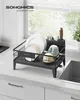 A black dish drying rack filled with dishes, cups, and cutlery is placed on a kitchen countertop next to a sink, with a window in the background. Produktbild-Vorschau
