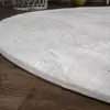 A close-up view of a fluffy white rug on a wooden floor. Produktbild-Vorschau
