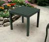 A dark gray square garden table is shown outdoors on a paved patio, with a flower bed in the background. Podgląd zdjęcia produktu