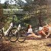 A couple is enjoying a picnic in a forest setting with two electric bikes nearby. Produktbild-Vorschau