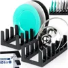 Two black dish racks are shown, one in the foreground and one slightly behind and to the left. The rack in the foreground holds two glass pot lids. The rack behind holds several plates, including a turquoise plate, a gray plate, and a black plate. A smalle Náhled obrázku produktu