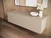 A beige lowboard with a white bowl and a vase of white flowers on top, set against a wooden wall and floor. Produktbild-Vorschau