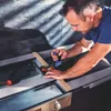 A man is using a clamp to hold a piece of wood in place on a workbench. Voir les images du produit