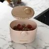A baby food container filled with granola and raspberries sits on a marble countertop. Produktbild-Vorschau