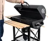 A person is holding the lid of a black charcoal grill with wooden side shelves. Náhľad obrázku produktu