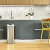 A modern kitchen with a stainless steel trash can, marble backsplash, and wooden cabinets. Anteprima dell’immagine prodotto