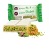 A white chocolate bar filled with pistachio cream and kadayif, with some pistachios and kadayif on the side, and two product packages in the background. Produktbild-Vorschau