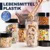 A collection of clear plastic food storage containers filled with various food items like pasta, cookies, candy, and cereal, with a person's hands holding tongs with pasta above one of the containers. Produktbild-Vorschau