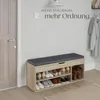 A shoe bench with storage in a hallway next to a door, with coats hanging on a rack in the background. Náhled obrázku produktu