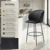 A black bar stool is shown in a modern kitchen setting, with text describing its features. Náhled obrázku produktu