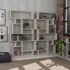 A modern white bookshelf unit displayed against a textured gray wall, with a rug and a purple ottoman in the foreground. Produktbild-Vorschau
