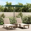 Two lounge chairs and a patio umbrella are set up on a paved patio area with lush green bushes and trees in the background. Náhled obrázku produktu