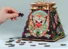 A hand is placing a puzzle piece onto a partially assembled wooden puzzle shaped like a pyramid with colorful artwork. Náhľad obrázku produktu
