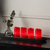 Four red LED candles and a vase with eucalyptus leaves are arranged on a black tray on a dark surface, with a white wall and molding in the background. Produktbild-Vorschau
