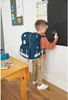 A young boy wearing a backpack is drawing on a blackboard. Voir les images du produit