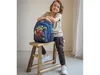 A young boy is posing with a Marvel Avengers backpack, sitting on a wooden stool. Produktbild-Vorschau