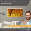 A man is pointing to a framed picture of autumn trees, which is mounted on a wall above a sofa. The image is part of an advertisement for an infrared heater. Produktbild-Vorschau