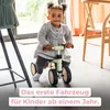 A young child is riding a small green balance bike indoors. Voir les images du produit