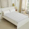 Weiße gesteppte Matratzenauflage mit Gummibändern auf einem weißen Bett mit zwei Kissen in einem hellen Schlafzimmer Náhľad obrázku produktu