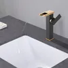 A close-up shot of a modern black and gold waterfall faucet installed on a dark gray marble countertop next to a white sink. Podgląd zdjęcia produktu