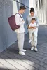 A family is standing on a paved walkway with a textured wall in the background. Produktbild-Vorschau