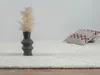 A shaggy rug with a diamond pattern pillow and a vase with dried flowers. Produktbild-Vorschau