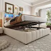 A bedroom scene featuring a bed with its storage compartment open, revealing stored items and a view of the headboard with LED lighting. Produktbild-Vorschau
