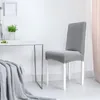 A gray chair cover is shown on a chair next to a small table with a plant and a blanket. Náhled obrázku produktu