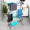 A black metal drying rack with multiple towels of various colors is set up in a bathroom with white tiled walls and a sink in the background. Produktbild-Vorschau