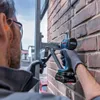 A person wearing safety gear is using a cordless impact wrench to attach a metal bracket to a brick wall. Voir les images du produit