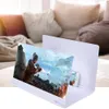 A smartphone screen magnifier is set up on a table, displaying a video game scene. In the background, a living room with a sofa is visible. Podgląd zdjęcia produktu