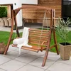 A wooden garden swing set with cushions and a blanket, placed on a patio next to a lawn and a house. Náhled obrázku produktu