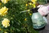 A hand wearing a glove is holding a green and black spray bottle and spraying a rose bush with yellow roses. Anteprima dell’immagine prodotto