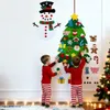 Two young children in pajamas are decorating a felt Christmas tree and snowman on a white wall. Produktbild-Vorschau