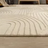 A close-up, low-angle view of a cream-colored rug with a geometric wave pattern, placed on a wooden floor. Produktbild-Vorschau