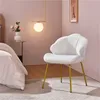 A white upholstered chair with gold legs is placed next to a bed in a room with pink walls. Produktbild-Vorschau