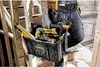 A construction worker carrying a tool bag up a wooden staircase. Anteprima dell’immagine prodotto